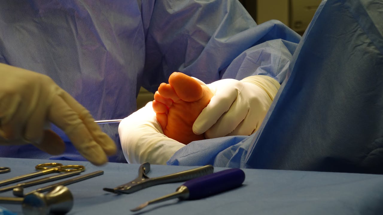 about-01 Gloved hands prepare for foot surgery in a sterile operating room environment.